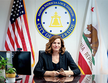 Mayor Patricia Lock Dawson at desk with, City of Riverside Seal, U.S.A and CA flags behind her 
